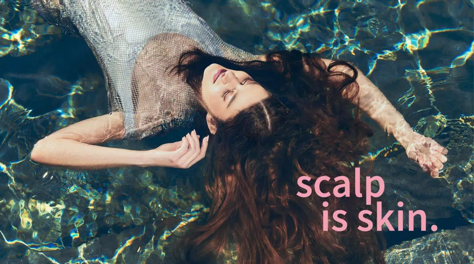 Vrouw met lang, glanzend haar drijvend in helder water, met de tekst “scalp is skin.”